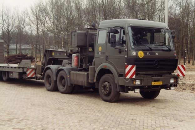 Ein Lkw mit einem Sattelauflieger steht vor einem Gebäude, umgeben von Bäumen und einem klaren blauen Himmel.