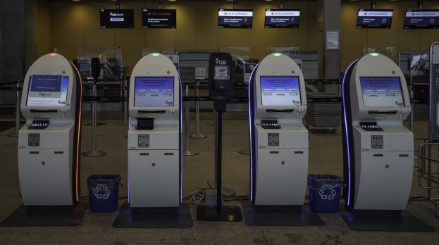 Eine Reihe von Geldautomaten auf einem gefliesten Boden mit Mülltonnen, Pfosten, bedruckten Plakaten, Lampen und anderen Gegenständen im Hintergrund.