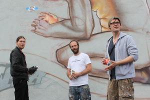 Menschen stehen und halten Farbsprühdosen in ihren Händen, mit einer Graffiti-bedeckten Wand dahinter.