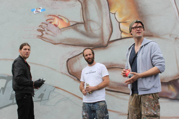 Menschen stehen und halten Farbsprühdosen in ihren Händen, mit einer Graffiti-bedeckten Wand dahinter.