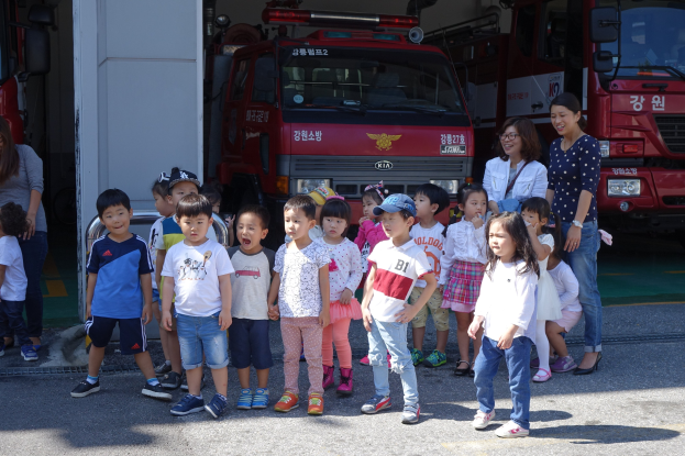 Eine Gruppe von Kindern vor mehreren Feuerwägen an einer Feuerwache, einige tragen Mützen.