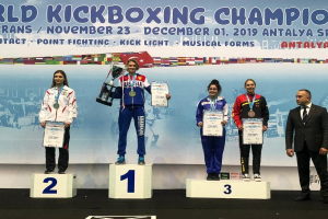 Fünf Personen auf einem Treppchen mit Trophäen und Urkunden in den Händen, im Hintergrund ein "World Kickboxing Championship Antalya 2019"-Plakat.