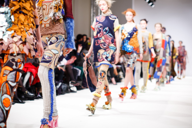Eine Gruppe Von Frauen Geht Auf Einem Laufsteg In London Fashion Week, Mit Sitzenden Zuschauern Und Bühnenbeleuchtung Im Hintergrund.