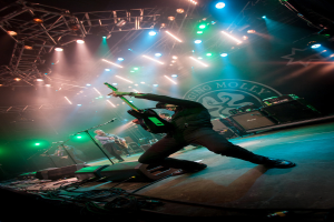 Ein musikalisches Konzert mit drei Performern auf der Bühne: zwei Gitarristen rechts mit Mikrofonen davor, ein Hintergrund mit "MOLLEY" und zwei Schlangensymbolen sowie Scheinwerfer darüber.