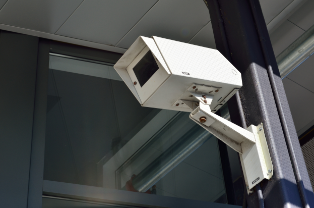 Eine Überwachungskamera auf einem Pfahl neben einem Gebäude mit einer Glastür im Hintergrund.