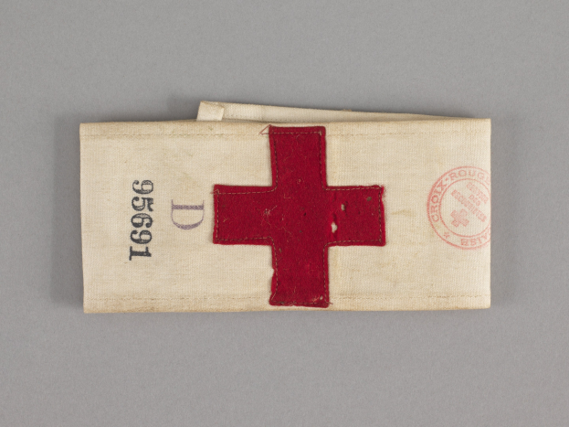 Ein rotes Kreuz-Ersthilfepaket in einem Stoffbeutel mit Text und einem Stempel, das auf einer Oberfläche liegt.