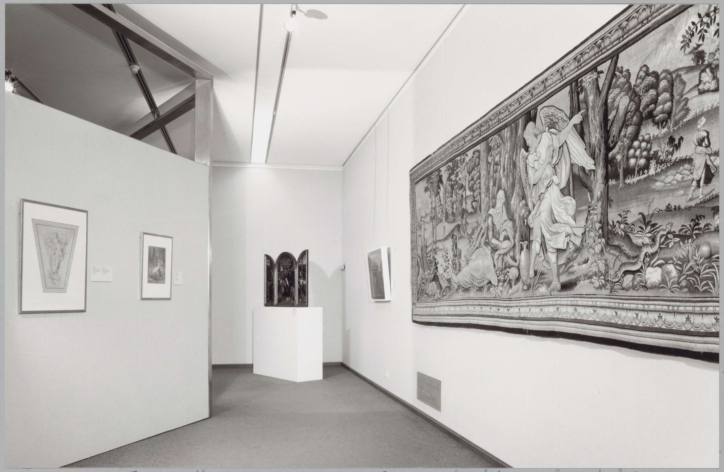 Schwarzes und weißes Foto einer Museumsgalerie mit einem großen Wandteppich, gerahmten Kunstwerken, Sockeldisplays und Deckenleuchten, wobei "Museum of Fine Arts, New York City" unten zu sehen ist.