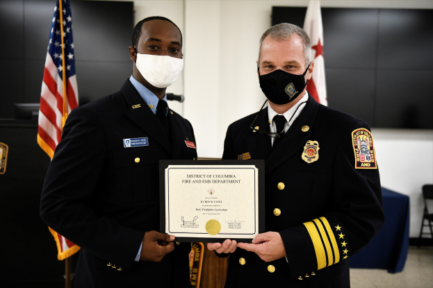 Zwei Männer in Feuerwehrausstattung stehen nebeneinander und tragen Masken sowie ein Zertifikat; der Mann links ist der Leiter der Feuerwehr des District of Columbia und erhält eine Auszeichnung.