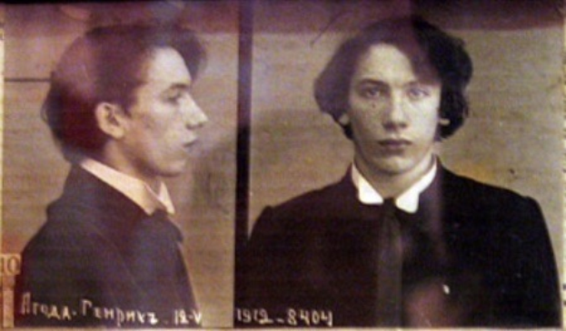 Ein Fahndungsfoto eines Mannes in schwarzem Anzug, weißem Hemd und schwarzer Krawatte mit ernstem Gesichtsausdruck und zurückgekämmtem Haar, begleitet von zwei zusätzlichen Fotos und fettgedrucktem Text über seine Verbrechen.