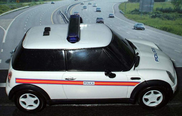 Weiße Polizeiwagen mit "Polizei"-Aufschrift auf einer Straße vor der Stadt, umgeben von fließendem Verkehr und grünen Bereichen mit Bäumen auf beiden Seiten.