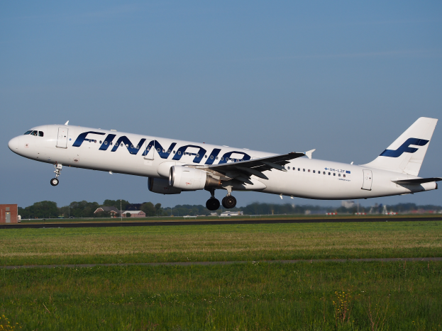 Ein Airbus A320-200 der Finnair startet von Frankfurt Airport, mit Gras darunter, Gebäuden und Bäumen im Hintergrund und einem klaren blauen Himmel darüber.