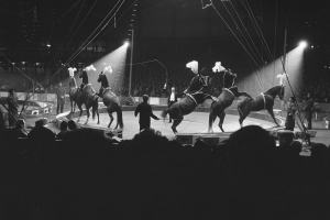 Schwarzes und weißes Foto von Darstellern auf Pferden auf einer Bühne mit Zuschauern und Crew im Vorder- und Hintergrund.