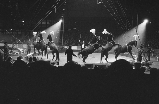 Schwarzes und weißes Foto von Darstellern auf Pferden auf einer Bühne mit Zuschauern und Crew im Vorder- und Hintergrund.