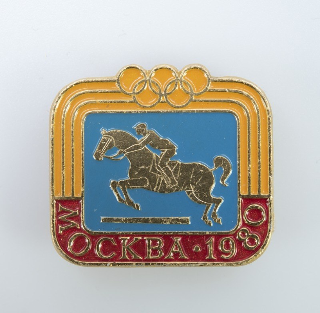Olympische Spiele-Badge aus den 1988er Winterspielen mit einer Person in weißem Hemd und blauen Shorts auf einem rotbraunen Pferd mit weißer Mähne und Schweif gegen einem hellblauen Himmel mit weißen Wolken.