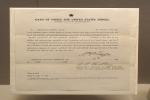 Ein Blatt mit dem Text "Dienstpflicht für US-Richter" liegt auf einem Tisch vor einer Wand.