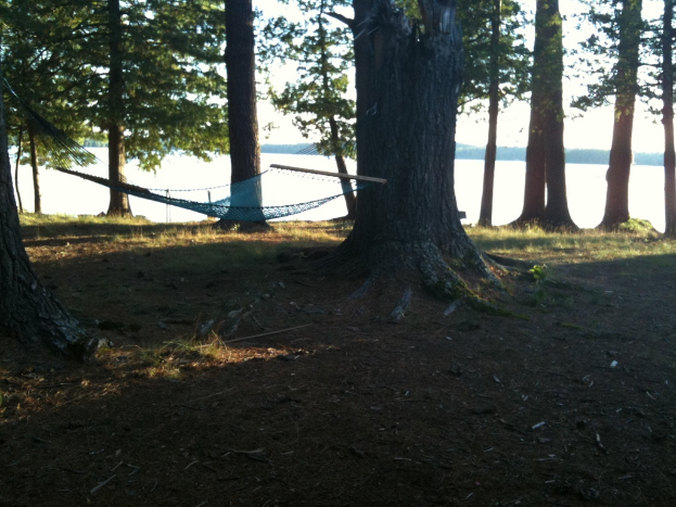 Ein Hängestuhl ist zwischen zwei Bäumen gespannt, mit Gras und Land unten und dem Meer im Hintergrund.