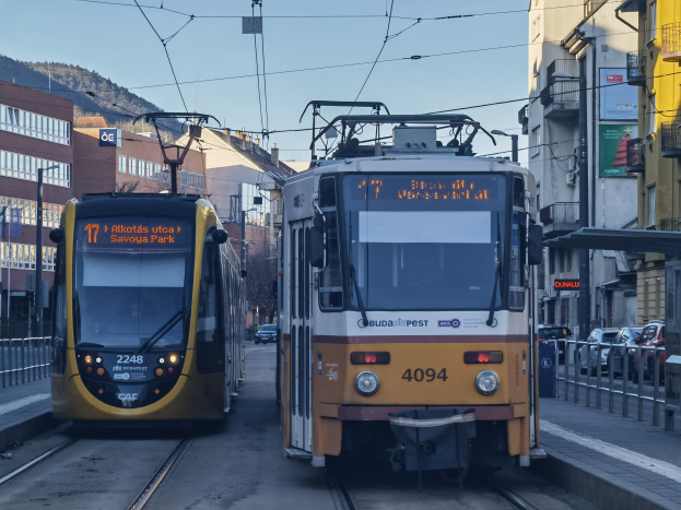 Zwei gelbe und weiße Straßenbahnen auf einer Stadtstraße mit hohen Gebäuden, Fahrzeuge auf der rechten Seite, Geländer auf beiden Seiten und einem Hintergrund aus Gebäuden, Polen, Schildern, Bäumen, einem Hügel und dem Himmel.