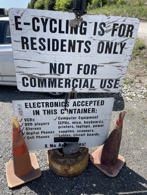 Schild mit Aufschrift "E-Bike-Fahren nur für Anwohner" neben einer Straße mit Verkehrskegeln, einem Fahrzeug, Bäumen und einem klaren blauen Himmel im Hintergrund.