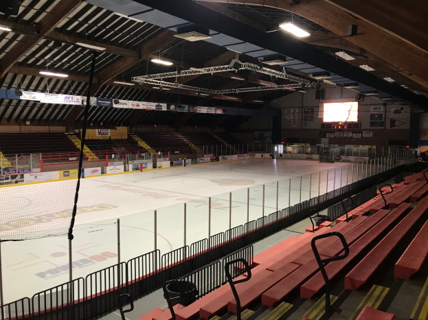 Eine große Indoor-Hockeyhalle mit Sitzplätzen, einem Zaun, einem Netz, Bannern, einem Bildschirm und Deckenleuchten, umgeben von verschiedenen Gegenständen.