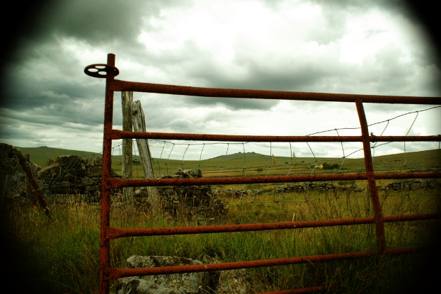 Eiserne Gitter mit Holzpfählen, Zaun, Hügel, Gras und einem bewölkten Himmel im Hintergrund.