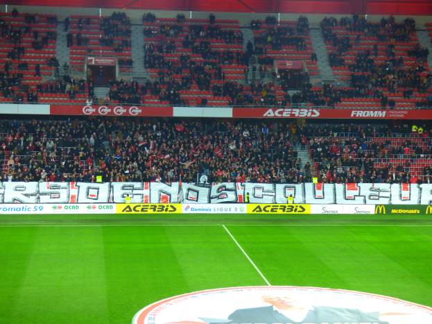 Ein Fußballfeld mit einer großen Zuschauermenge auf den Rängen, umgeben von Texttafeln und einem Logo mit Text unten.