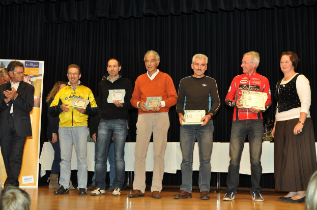 Eine Gruppe von Menschen auf einer Bühne mit Urkunden in der Hand, im Hintergrund eine Tafel, ein Tisch daneben und ein schwarzer Vorhang.