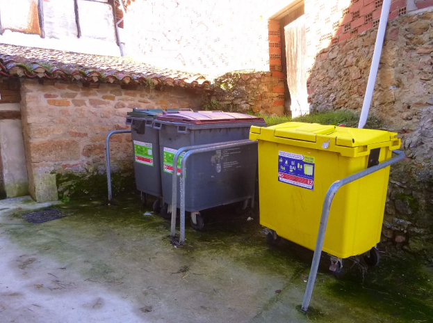 Zwei gelbe und graue Mülltonnen auf Rollen stehen nebeneinander vor einem Gebäude mit einer Wand und einem Fenster im Hintergrund.