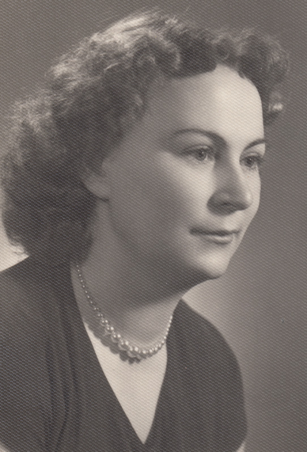 Ein Schwarz-Weiß-Foto einer Frau mit ernstem Gesichtsausdruck, die eine Kette und ein einfaches Kleid mit hohem Kragen und langen Ärmeln trägt, ihr Haar ist zurückgebunden.