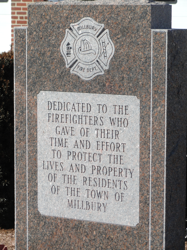 Ein Gedenkstein mit einer Plakette vor einem Backsteingebäude, umgeben von Pflanzen und Bäumen, gewidmet den Fürsten von Millbury.