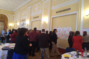 Eine Gruppe von Menschen untersucht Plakate und Diagramme, die an einer Wand in einem Raum aufgehängt zu sein scheinen, der wie ein Kunstmuseum aussieht.