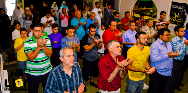 Menschen beten in einem Saal, mit Text in der unteren linken Ecke.