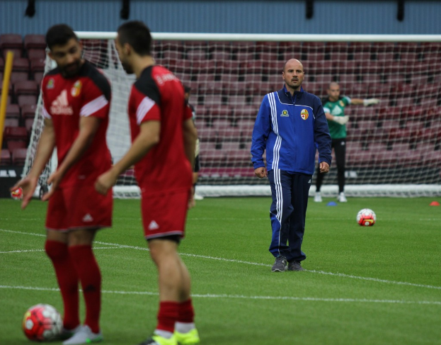 Ein Fußballfeld mit Spielern darauf, zwei Bälle und eine leere Tribüne im Hintergrund.
