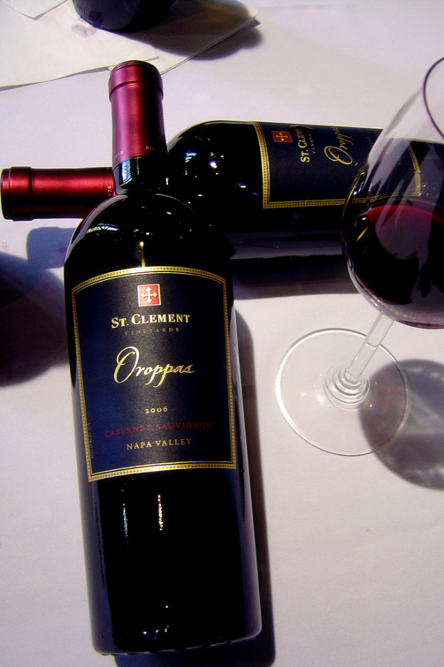 Zwei Flaschen, ein Glas mit Getränk, mehrere Umschläge und ein unbekannter Gegenstand auf einer Oberfläche.