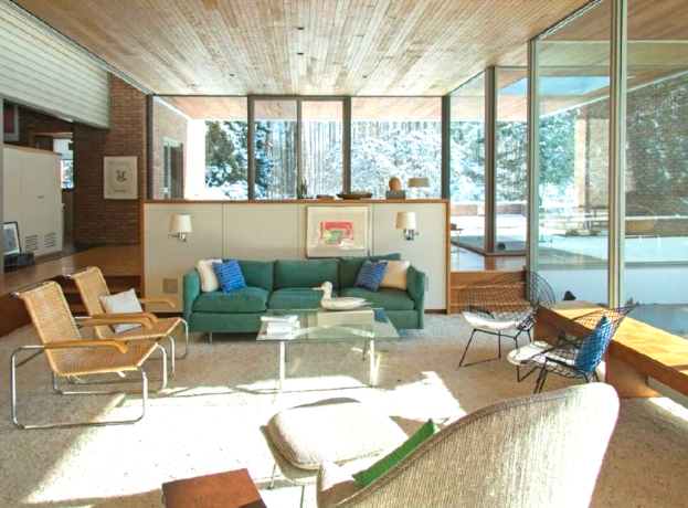 Ein Sofa mit Stühlen auf der linken Seite, eine Glaswand auf der rechten Seite und ein offener Raum in der Mitte.