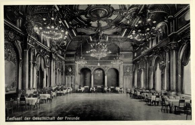 Schwarz-weißes Foto eines großen Raums mit Tischen, Stühlen, Säulen, Bögen und Kronleuchtern, beschriftet mit "Fest der Gesellschaft der Freunde, Berlin" unten.