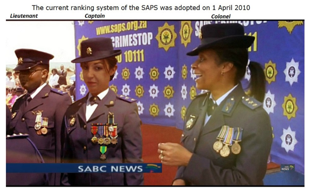 Gruppe von Menschen in Uniformen und Hüten, die mit einem Banner stehen, mit Text oben und unten, der besagt: "Das aktuelle Ranglistensystem der SAP wurde am 1. April 2010 eingeführt."