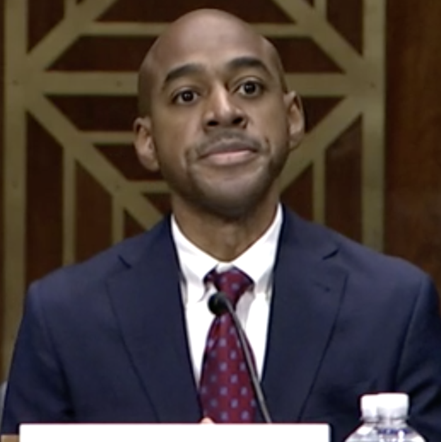 Ein Mann im Anzug und Krawatte sitzt an einem Tisch mit Namensschild, Mikrofon und Wasserflasche und Aussagen vor dem Senatsjustizausschuss auf dem Capitol Hill.