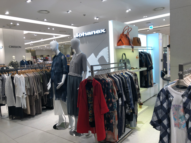 Ein Modegeschäftsinneres mit Schaufensterpuppen, Kleiderstangen, Handtaschen, Beschilderung, Deckenleuchten und einer Säule, das im Mall of Asia zu finden ist und Teil der Johanex-Marke ist.