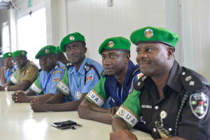 Gruppe von Polizeibeamten sitzt an einem Tisch mit Mobiltelefonen und anderen Gegenständen während einer Schulung in einem Raum mit Fenstern und Deckenleuchten.