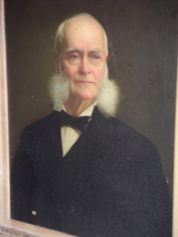 Ein Schwarz-Weiß-Porträt eines älteren Mannes mit einem weißen Bart und Brille, der einfache, zeitlose Kleidung trägt und in einem Foto Rahmen.