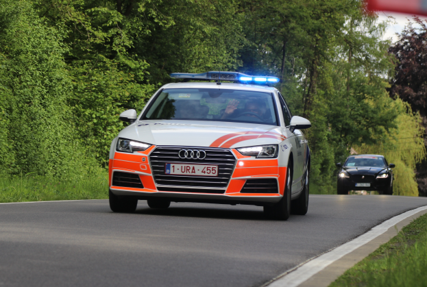 Ein Polizei-Audi A4 fährt eine Straße neben einem Wald entlang, mit zwei Personen darin, Gras auf beiden Seiten und einem klaren blauen Himmel im Hintergrund.