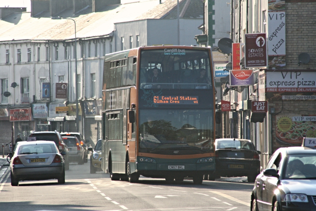 Eine StraÃe mit Autos und einem Bus vor GebÃ¤uden mit WÃ¤nden, Fenstern, Tellern und DÃ¤chern, mit Plakaten und Bannern an den WÃ¤nden und einem Pfahl mit einer StraÃenlaterne.