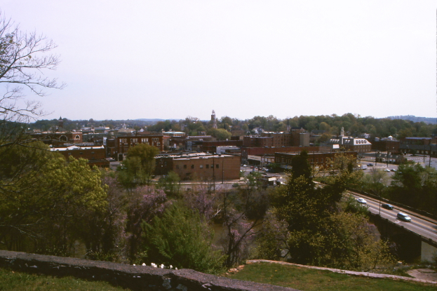 Stadtpanorama mit Gebäuden, Bäumen, Pfählen, Straßen, Fahrzeugen und Himmel.