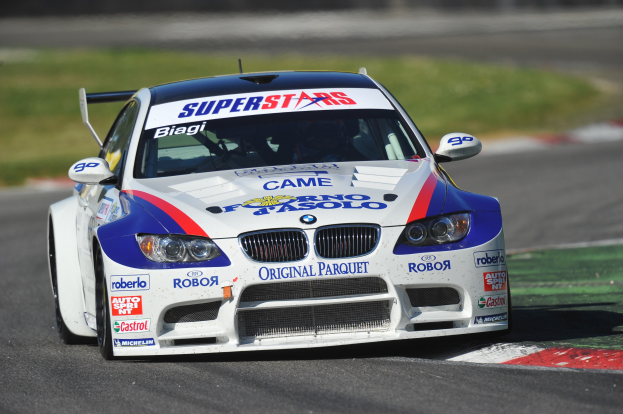 Ein BMW M3 GT3 Rennauto auf einer unscharfen Rennstrecke mit Gras im Hintergrund.
