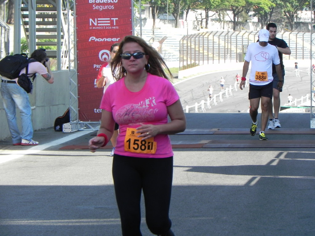 Menschen laufen auf einer Straße mit einem Banner auf der linken Seite, Treppen hinter dem Banner und Bäumen, Gebäuden und einem Metallzaun im Hintergrund.