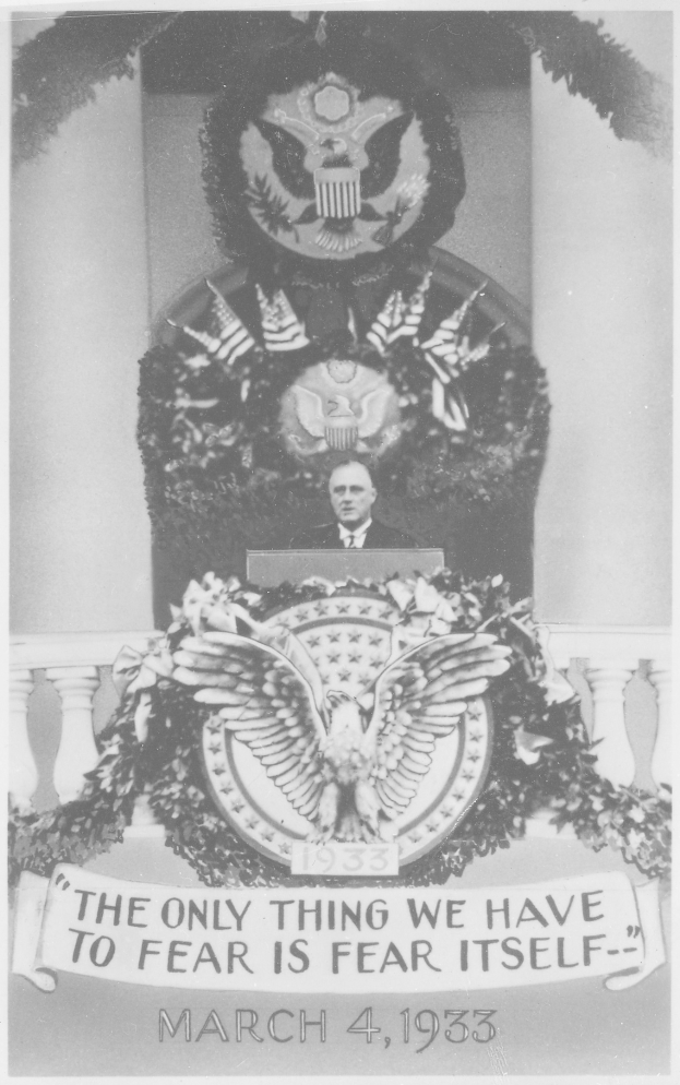 Schwarzes und weißes Foto eines Mannes, der an einem Rednerpult spricht, mit einem Kranz und einem Emblem an der Wand dahinter, Text unten lautet "Das einzige, wovor wir uns fürchten müssen, ist die Furcht selbst."