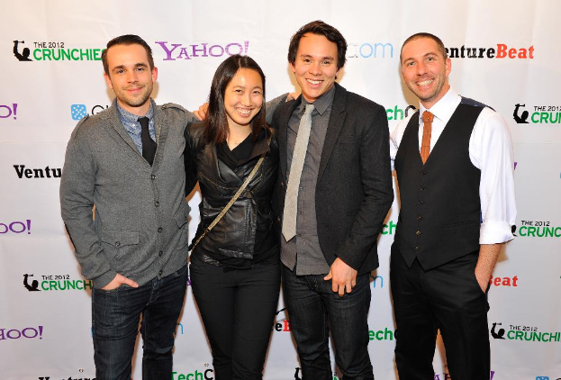 Eine Gruppe strahlender Menschen, die mit einem Sponsorenbanner im Hintergrund für die Kamera posieren.