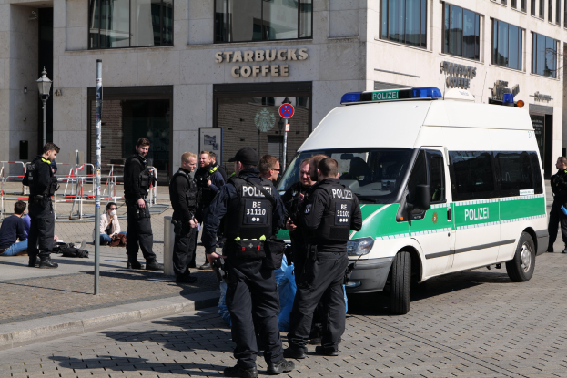 Gruppe von Polizeibeamten vor einem Starbucks-Café mit einem Van auf der rechten Seite und Menschen auf der linken Seite, Hintergrund enthält ein Gebäude, ein Schild, einen Laternenmast und eine Absperrung.