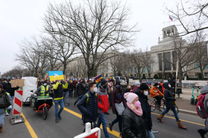Eine große Gruppe von Menschen marschiert auf einer Straße in Washington, D.C. am 21. Januar 2020 mit Schildern und Bannern, einige fahren Fahrräder, Schilderstände mit Ständen, Bäume und einen klaren blauen Himmel im Hintergrund.