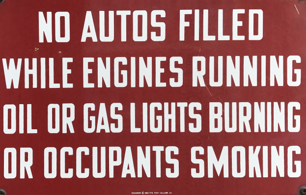 Ein rotes Schild mit weißer Schrift, das warnt: "Keine Autos betanken, während der Motor läuft, Öl- oder Gaslichter brennen oder Insassen rauchen."